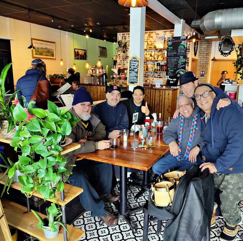 Six men smiling and posing for a photo at a wooden table inside a cozy restaurant.